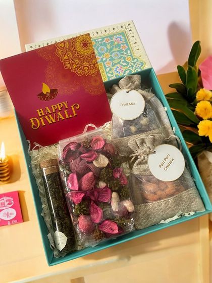 For those who love soothing gifts, this hamper is perfect. It includes fragrant potpourri, a tube of premium green tea, and small jute bags of cashews and trail mix, all presented in a lovely turquoise box.