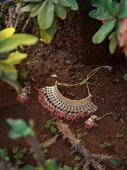 A creative shot of the bride's necklace and earrings, laid out on the ground amidst nature. This photo highlights the beauty of the bridal jewelry.