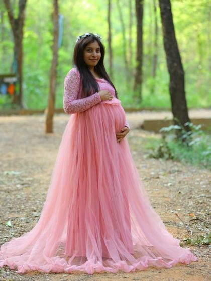 This light pink maternity gown features delicate lace sleeves and a long tulle train. It's a romantic and feminine choice for an outdoor photoshoot in the woods.
