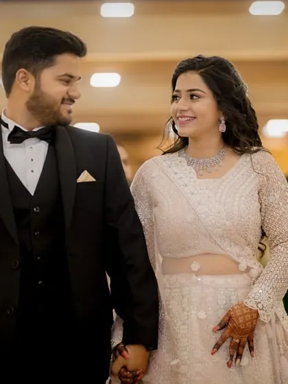 Dressed in elegant evening wear, the couple walks hand-in-hand at their engagement party, looking at each other with adoration.