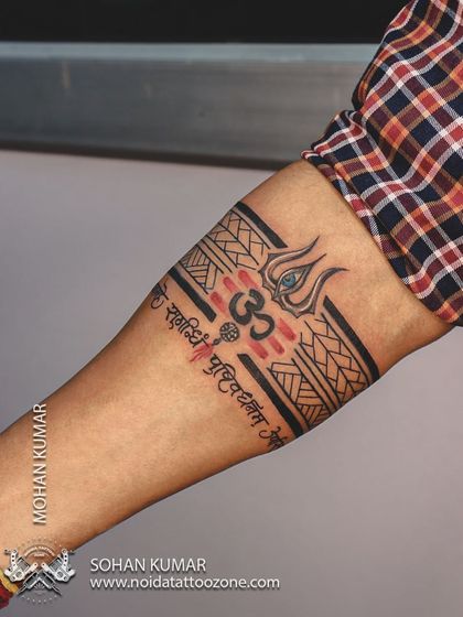 This is a custom band tattoo with a Lord Shiva theme. It incorporates a Trishul, the Om symbol, and the Mahamrityunjaya mantra into a single, cohesive armband design with red and black ink.