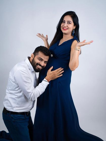 A playful and happy moment. The dad-to-be listens to the baby bump with a big smile, while the mom-to-be looks on with joy.
