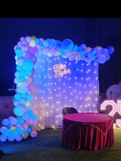 A 'Better Together' themed backdrop for an anniversary or engagement party. This outdoor setup includes a balloon arch, a curtain of fairy lights, and a light-up number '25'.