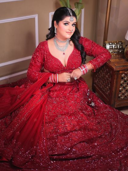A glamorous seated portrait that captures the full splendor of the red lehenga.