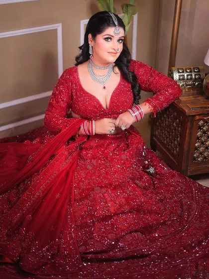 A full-body seated portrait showcasing the magnificent spread of the sequined red lehenga.