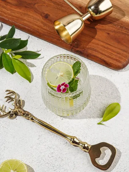 A minimalist product shot of a deer-head bottle opener and other bar accessories, styled with fresh lime and mint for a refreshing summer feel.
