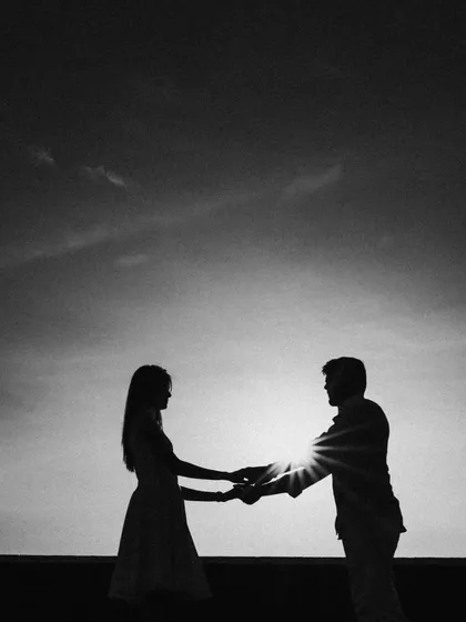 A striking black and white silhouette of a couple against the setting sun. The sunburst effect adds a dramatic flair to this classic and timeless romantic pre-wedding photo.