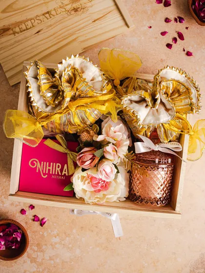 An overhead shot of the open 'PHOOL' hamper, revealing its contents. This perspective shows the careful arrangement of the festive items inside the wooden crate, including sweets, potlis, and floral decorations.