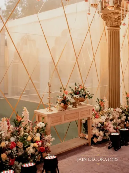 A beautiful corner where classic elegance meets rustic charm. A wooden console table is surrounded by lush floral arrangements, set against a softly lit, textured backdrop.