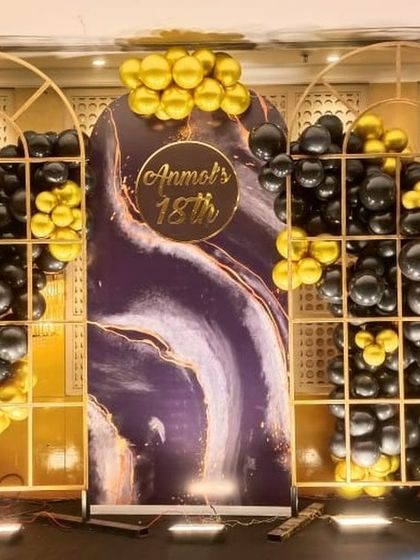A grand and artistic backdrop for an 18th birthday, using arched panels with a marble design and clusters of black and gold balloons.
