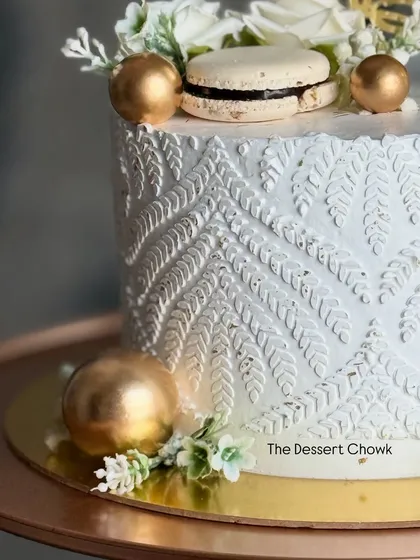 A close-up of the beautiful stencil work and macaron detail on the white and gold anniversary cake.