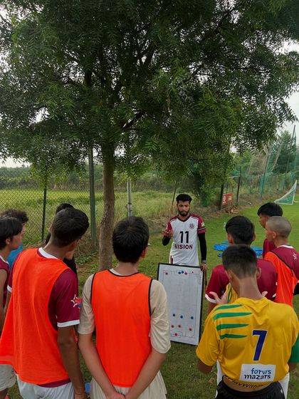 A coach explains positioning and movement to the team using a tactical board during a training session. We ensure our players understand the 'why' behind every drill.