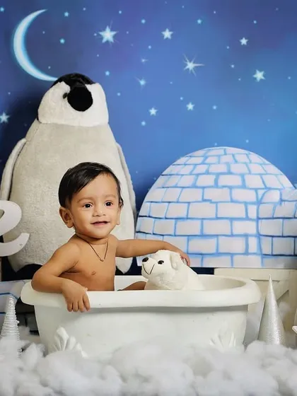 A fun, arctic-themed photoshoot with penguins and igloos. This little one is enjoying a "bath" in the snow, creating a unique and imaginative scene.