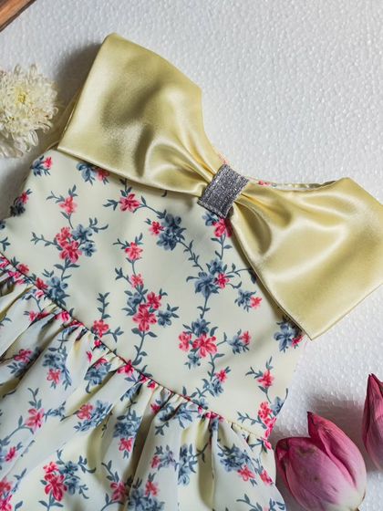 A closer look at the gathered construction of this yellow floral dress. The satin collar is adorned with a sparkling sequined ribbon for an extra touch of glamour.