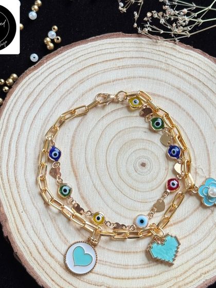 A stylish bracelet-style rakhi for the trendy kid. It features multiple evil eye charms, hearts, and flowers on a gold chain, making it a piece they can wear all year.