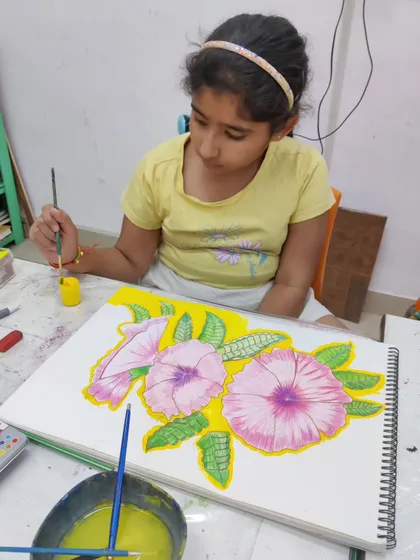 A young student carefully paints a floral composition, learning to control the water and pigment to create soft, blended colors.