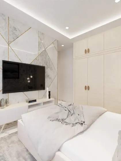 In this bedroom, I designed a feature wall with white marble-finish panels and gold inlay for the TV area. The clean, handleless wardrobes provide ample storage while maintaining a minimalist and spacious look.