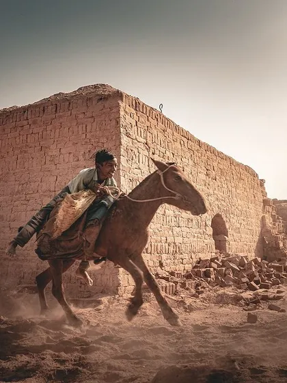 A young worker and his horse kick up dust at a brick kiln in Bihar. I use monochrome to emphasize the timeless, cinematic quality of daily labor, focusing on the motion and grit of their story.