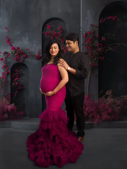 A beautiful couple's shot against a modern, textured backdrop with pops of magenta flowers. The image captures the love and partnership of the journey into parenthood.