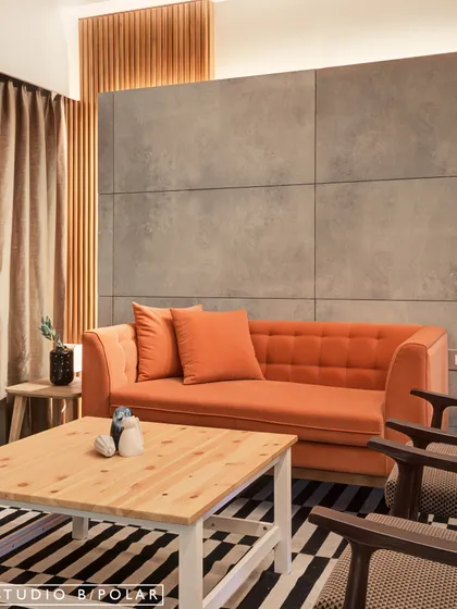 A wider view of the space, showing how the industrial feel of the concrete panels is balanced by the warmth of the orange sofa and the natural wood coffee table.
