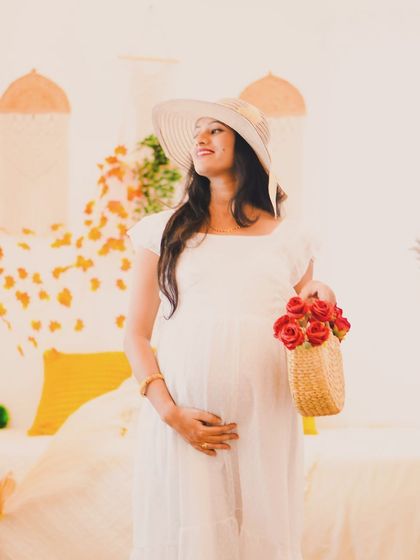 A stylish solo maternity shot in a simple white dress. The wide-brimmed hat and basket of roses add a touch of rustic elegance to this photo in the Boho set.