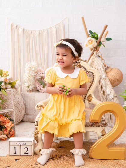 A sunny second birthday. This little girl in her bright yellow dress is all smiles as she celebrates turning two in a cheerful, rustic setting.