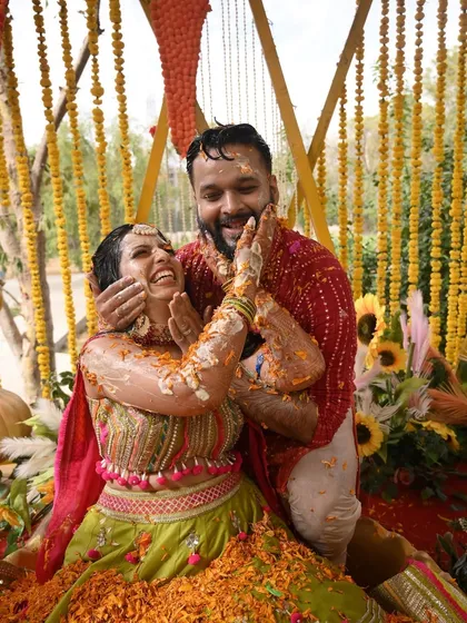 A candid moment of pure fun during a Haldi ceremony. The couple's joy is infectious as they celebrate amidst a backdrop of hanging marigold strings, a classic element of traditional Haldi decor.