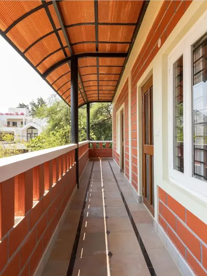 A long, covered verandah with a curved terracotta tile roof provides a perfect transitional space, offering shelter while remaining open to the garden.
