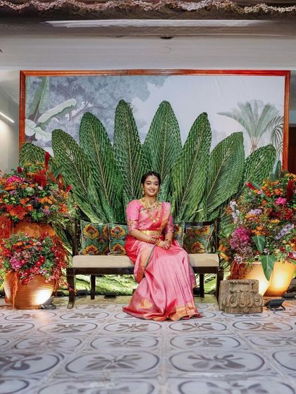 The bride seated for her Pellikuthuru ceremony against the stunning woven coconut leaf backdrop.