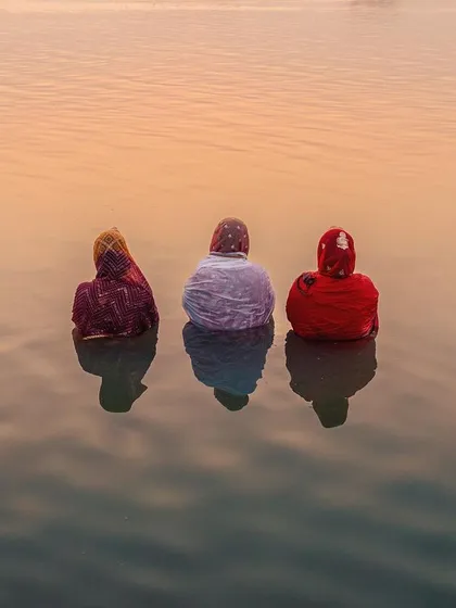 Three women offer prayers during Chhath Mahaparv in Bihar, their forms reflected in the calm water at dusk. This image captures the quiet, painterly beauty of faith, a moment of pure tranquility and devotion.