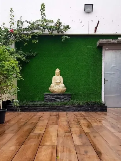 A tranquil patio space with a wooden deck, an artificial grass wall, and a Buddha statue as the focal point. This creates a perfect spot for meditation or quiet relaxation.