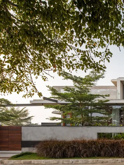 The entrance to The Quarry House is framed by a concrete boundary wall and a warm timber gate. The landscaping, with its mix of grasses and trees, softens the modern structure and roots it in its site.