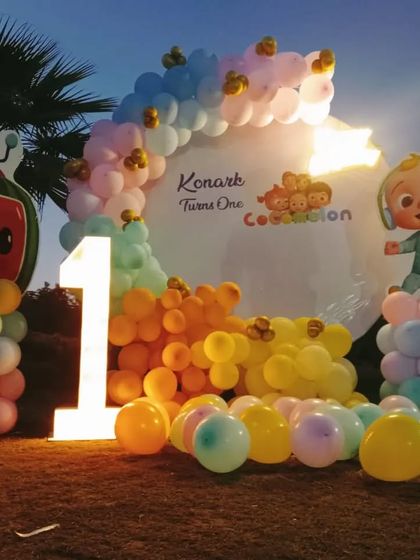 An outdoor Cocomelon party for a first birthday. This decoration uses a pastel balloon arch and character cutouts to create a fun and inviting space for the little ones.
