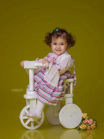 A simple and classic portrait of a little girl on a white tricycle. The solid green-yellow background makes her striped dress and happy face the center of attention.