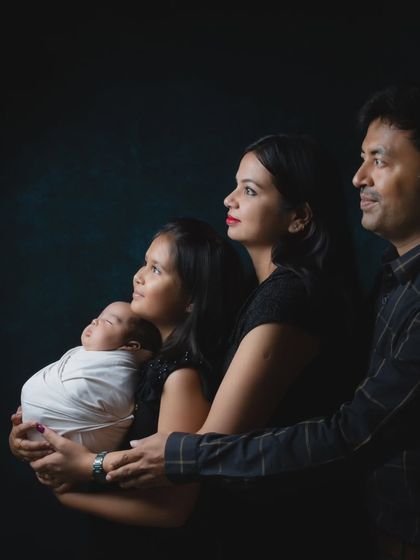 A classic family photo featuring a newborn, older sister, mother, and father in a beautifully lit studio setting.