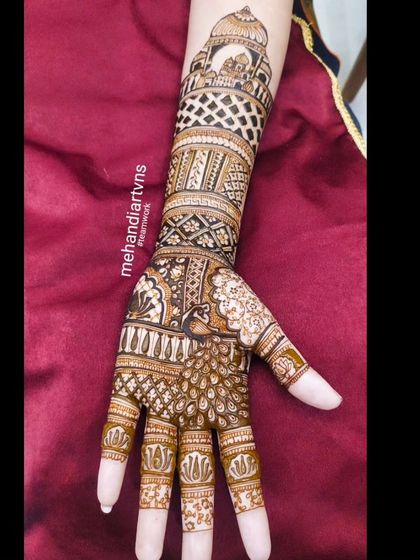 A single arm view of a design featuring a majestic peacock on the hand and an architectural dome at the top, connected by bands of intricate patterns.