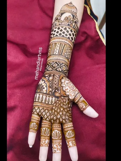 A single arm view of a design featuring a majestic peacock on the hand and an architectural dome at the top, connected by bands of intricate patterns.