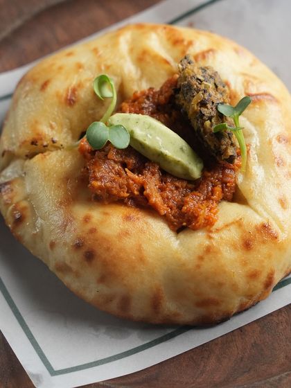 Our Pulled Duck Kulchette, a small, fluffy bread topped with tender pulled duck, herb butter, and a tangy tapenade pickle. A sophisticated and flavourful bite.