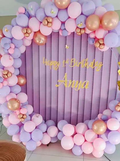 A simple and beautiful butterfly-themed decoration for Anya's first birthday. The design features a circular backdrop with a purple fabric cover and a pink and lavender balloon arch.