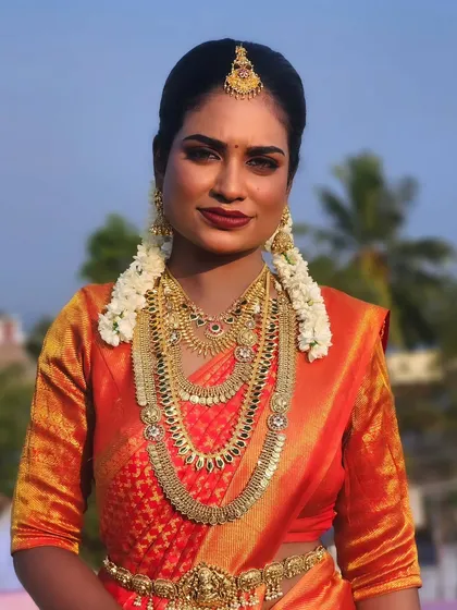 A full-length portrait of a dusky bride in a vibrant orange saree. The makeup is bold and beautiful, and she looks absolutely stunning.