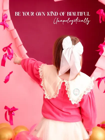 A shot from behind shows a little girl with a large white bow, pointing at the heart-themed backdrop. The text "Be your own kind of beautiful" adds an empowering message to this sweet photo.