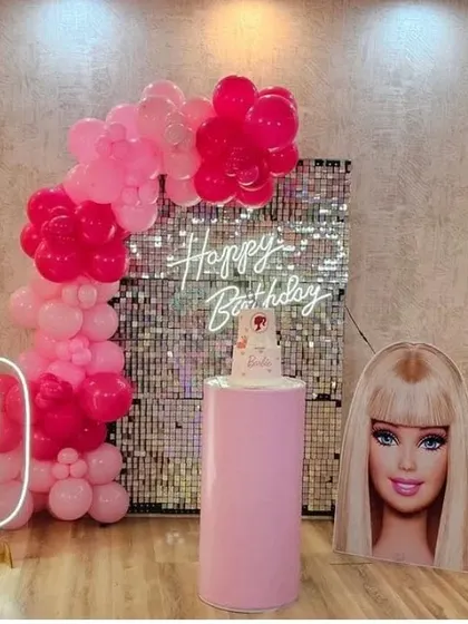 A chic Barbie theme for a 9th birthday. This setup includes a pink sequin wall, a Barbie head cutout, a marquee number '9', and a pink balloon garland.