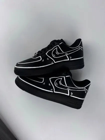 A pair of all-black Nike Air Force 1s given a striking cartoon effect with bold white outlines.