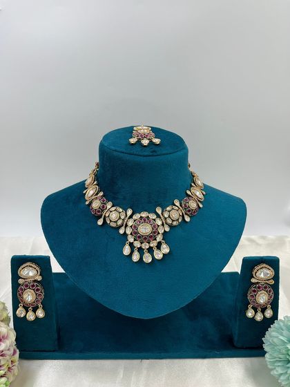 A pair of Moissanite Kundan earrings with a circular design. The ruby-colored stones and white stone drops make these a vibrant and attractive choice.