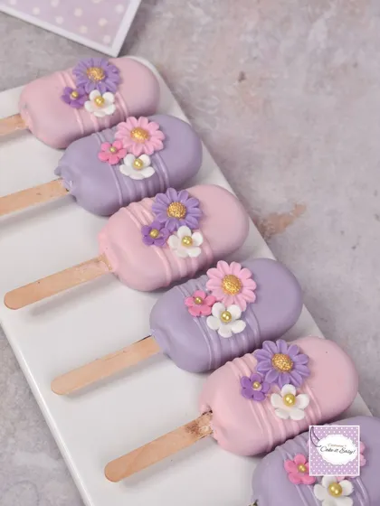 Fairy garden themed cakesicles in pastel pink and purple, decorated with tiny sugar flowers.