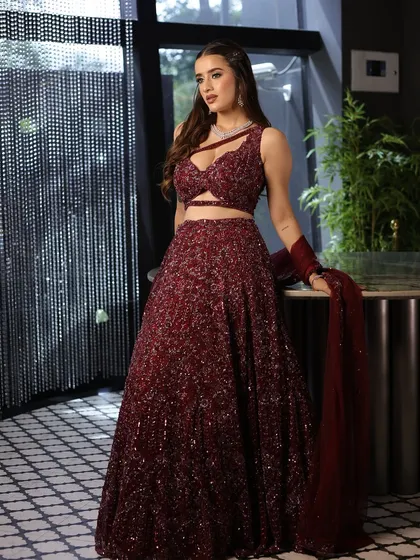 A full-length shot of the bride in her magnificent maroon sequin lehenga. The makeup is glamorous yet sophisticated, perfect for a cocktail night.