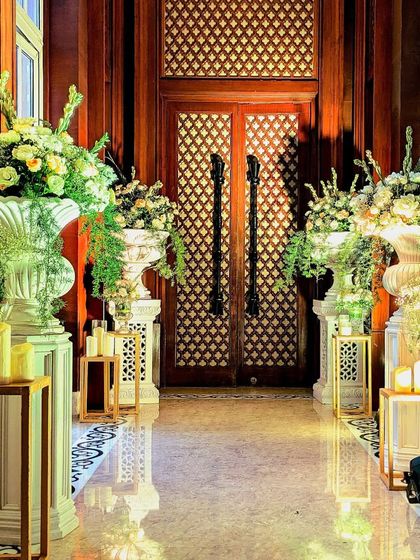 An elegant hallway at the ITC Maratha, lined with classic white urns filled with lush white and green floral arrangements. The design creates a grand and stately passage for guests.