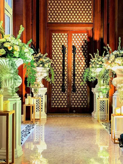 The indoor entrance corridor was lined with classic white urns, lush floral arrangements, and warm candlelight, guiding guests into the main event with grace and style.
