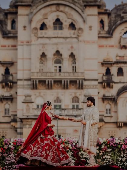 The couple on stage, surrounded by a sea of flowers, with the palace as their backdrop.