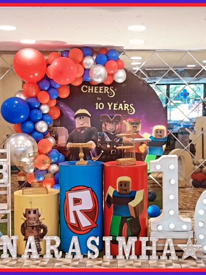 A gaming-inspired Roblox-themed 10th birthday party. The setup includes character cutouts, a 'Cheers to 10 Years' backdrop, and a large light-up number '10'.